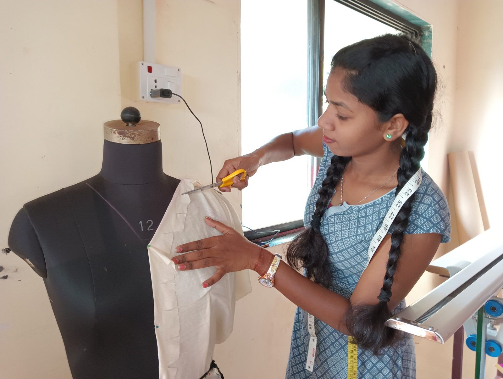 A student draping muslin on a dress form in the B.Design studio, tape measure around her shoulders